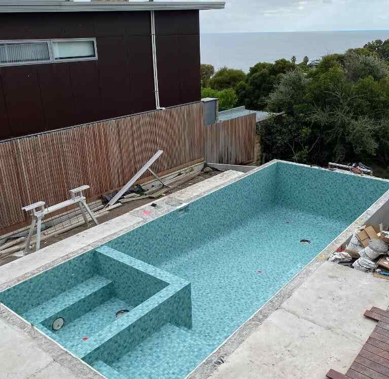 Backyard swimming pool construction in progress with blue mosaic tiles