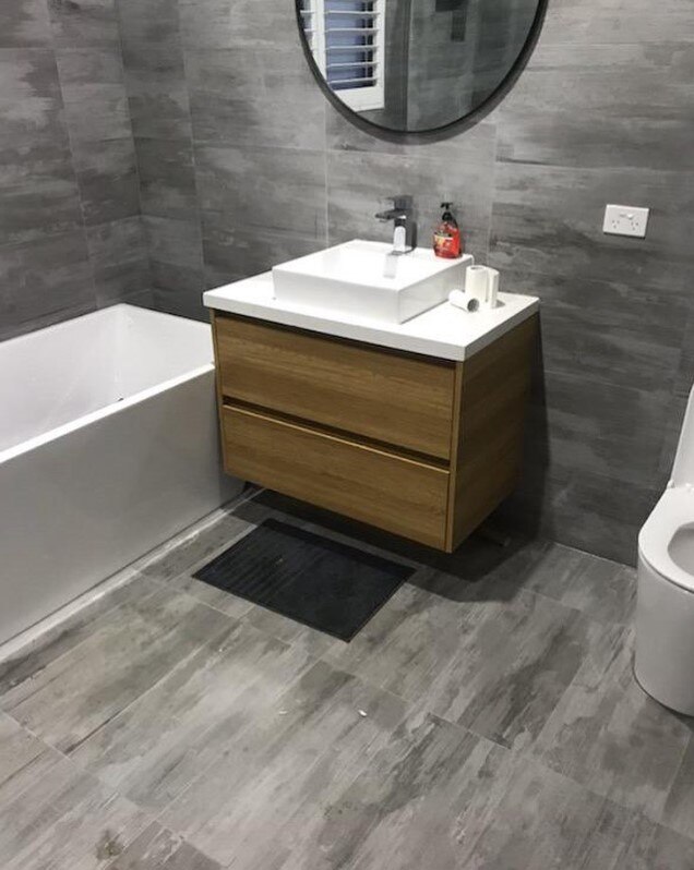 Modern bathroom featuring sleek wood vanity, white sink, round mirror, and minimalist tub.