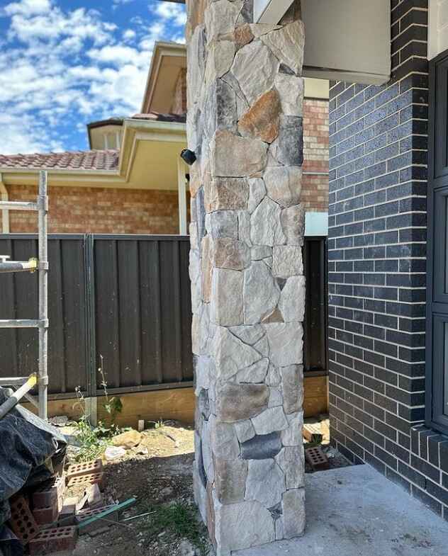 A sturdy exterior column with natural stone cladding beside a dark brick wall under construction