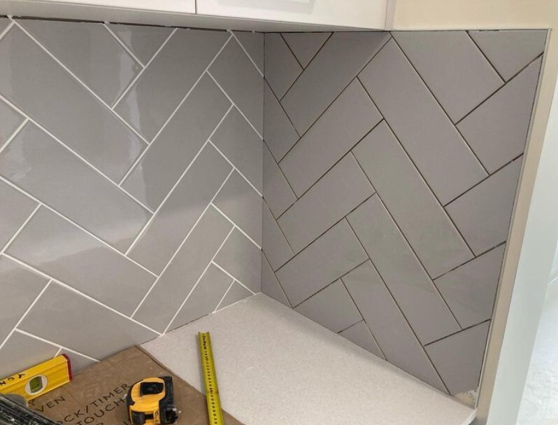 Ongoing installation of light gray herringbone tiles in a modern room, showing precision and craftsmanship.