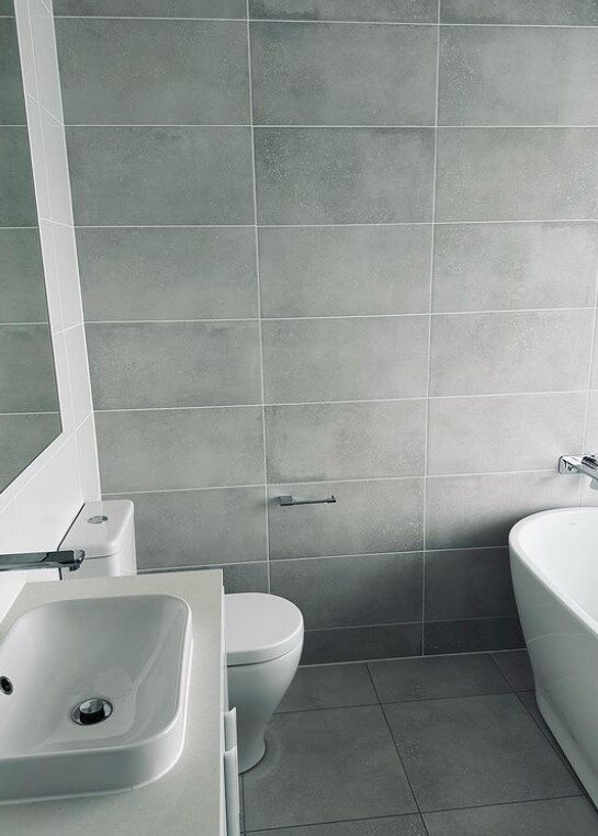 Minimalist style bathroom with large grey tiles, white toilet, and bidet, showing a modern and simple design