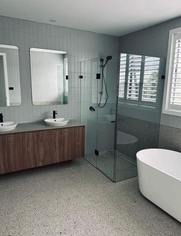 A contemporary bathroom featuring a double sink vanity and a clear glass shower enclosure with grey tiles