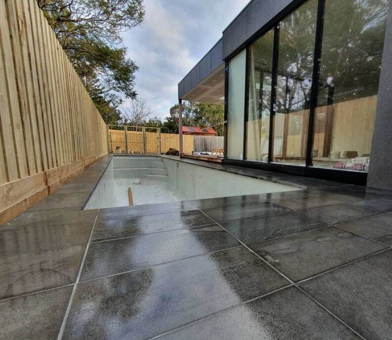 Modern patio with reflective tiles, glass wall, and wooden fence, showcasing sleek design and natural elements.