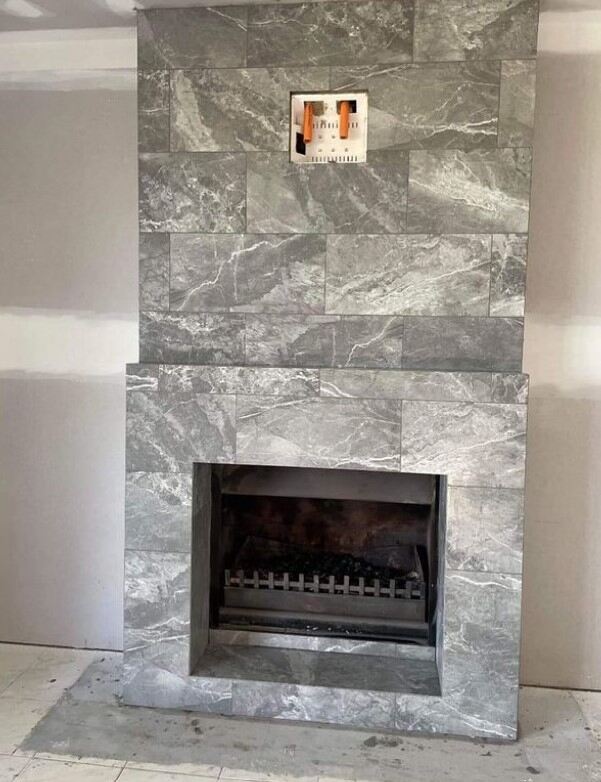 Modern fireplace with grey marble tiles and decorative art above, in a minimalist setting.