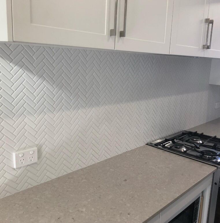 Modern kitchen featuring light grey countertop and herringbone tile backsplash, sleek and spacious.