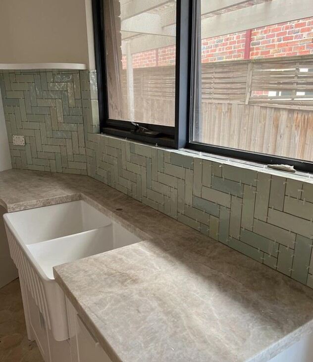 Modern kitchen corner featuring marble counters and seafoam green subway tiles.