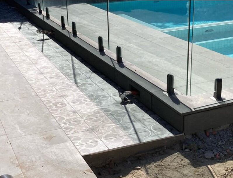 Modern pool design featuring a transparent glass wall and ornately patterned tiles.