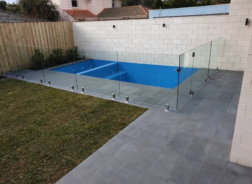 Contemporary Australian pool deck with glass fencing and lawn.