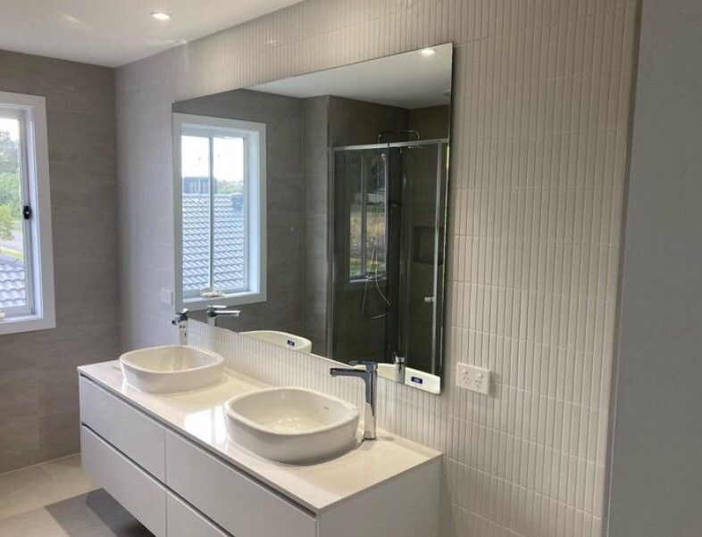 Modern bathroom with sleek gray tiles, dual sinks, and large mirror illuminated by natural light.