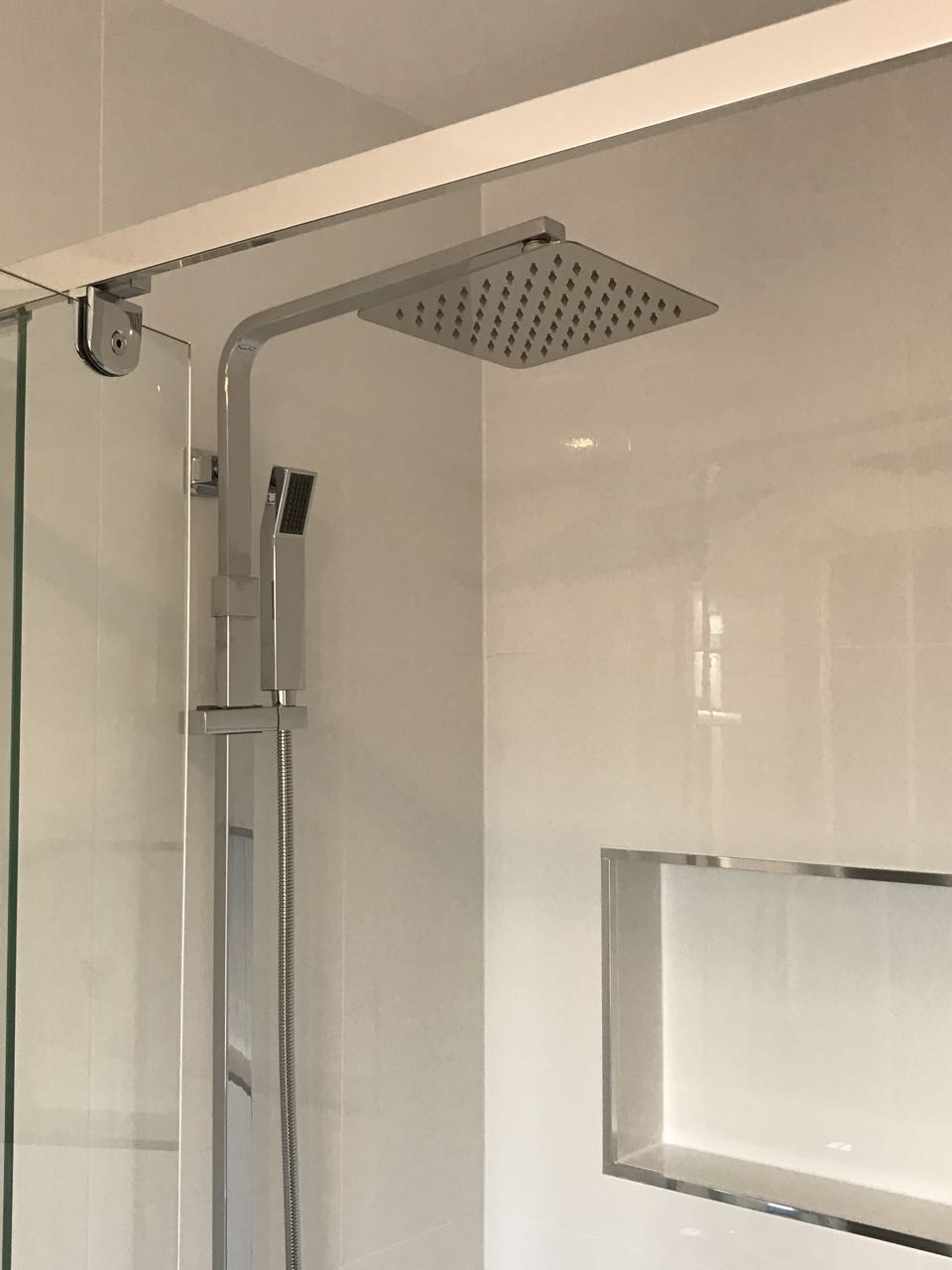 Sleek stainless steel rain shower head with a handheld sprayer in a modern bathroom with glass doors